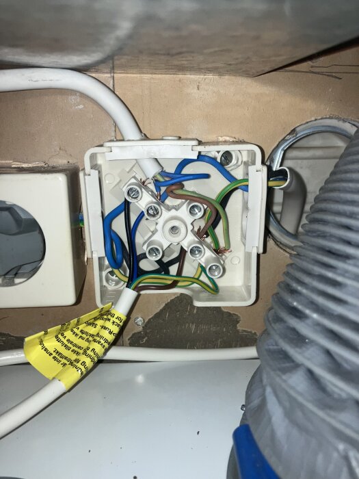 Elkopplingsplint med flera kablar i olika färger, placerad under en diskbänk, intill en strömbrytare och ventilationsrör.