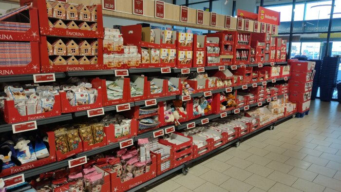 Hylla med julkakor och sötsaker i en butik, där röda kartonger med olika produkter är uppställda för försäljning.