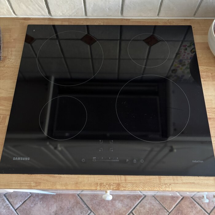 En svart induktionshäll av märket Samsung med fyra kokzoner på en köksbänk.