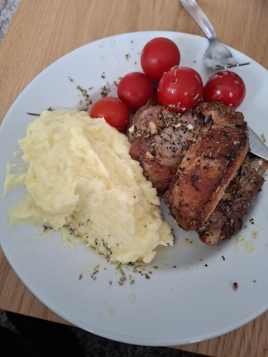 Tallrik med tjocka revbensspjäll, potatismos och körsbärstomater.