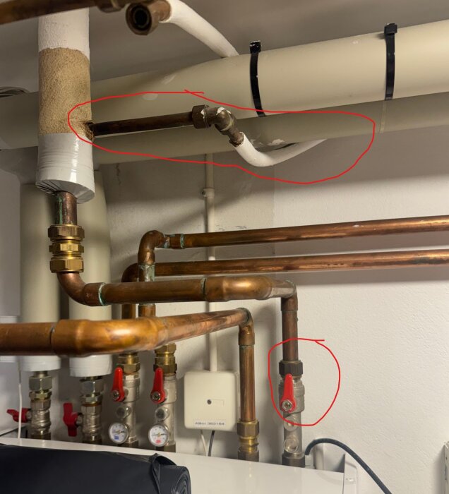 Vattenrör och ventiler i källare med inringad sektion för inkommande vatten. Flera kopparrör och röda ventilreglage synliga.