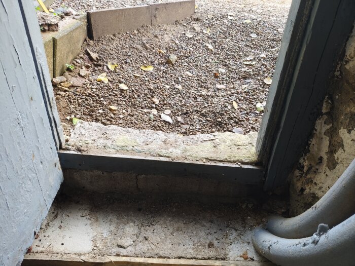Ingång till källare med betongtröskel och grus utanför; oavslutad yta som behöver återställas efter vatteninstallation i bod.