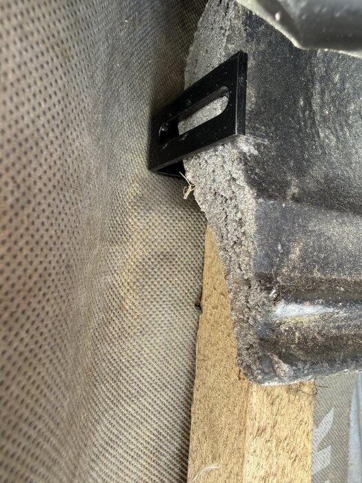 Närbild av en svart takpanna med ett metallfäste monterat, synligt trä och takunderlag i bakgrunden.