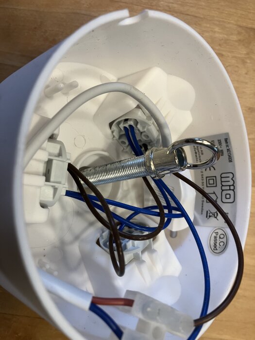Taklampa från insidan med metalldel för upphängning och flera elledningar. Märkt CE och "Passed Q.C." synligt på etiketten.