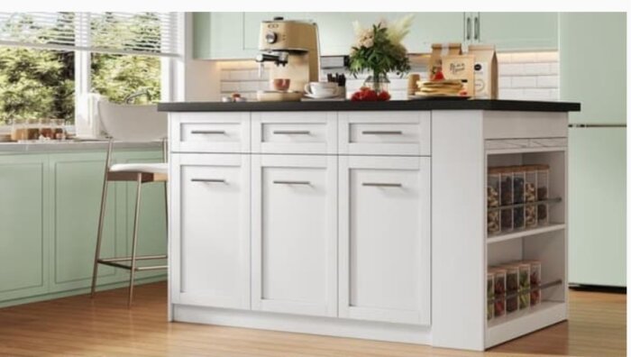 Köksö med vit skåpsinredning, svart bänkskiva, och förvaring på sidan, står i ett kök med mintgröna skåp och ett stort fönster.