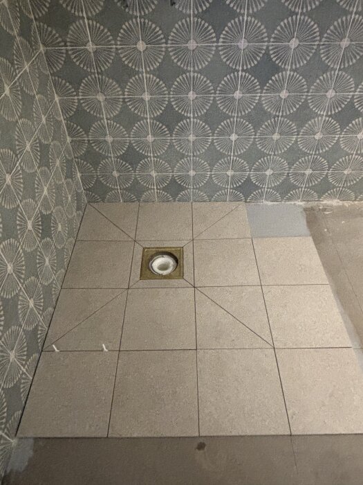 Golvet visar nyfixerad kuvertskärning med fyrkantiga kakelplattor och ett golvavlopp, redo för fortsatt arbete.