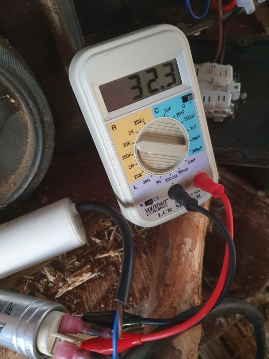 Multimeter visar 32,3 uF, mäter kondensator kopplad med ledningar, omgivande verktyg och trä.