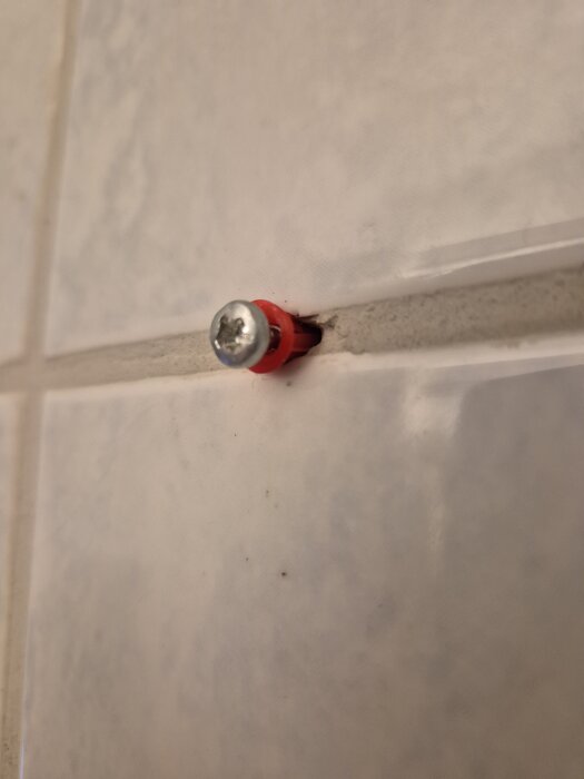 Skruv med röd plugg som sitter i kakelfog i ett badrum.