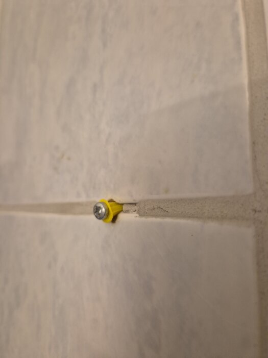 Skruv med gul plugg i kakelvägg i badrum, oro över korrekt installation och våtzonssäkerhet.