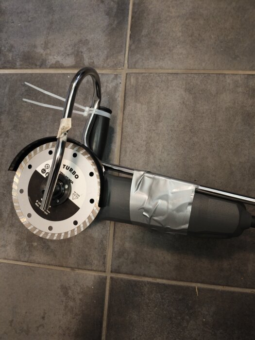 Vattenkyld vinkelslip med silvertejp, liggande på ett grått kakelgolv.