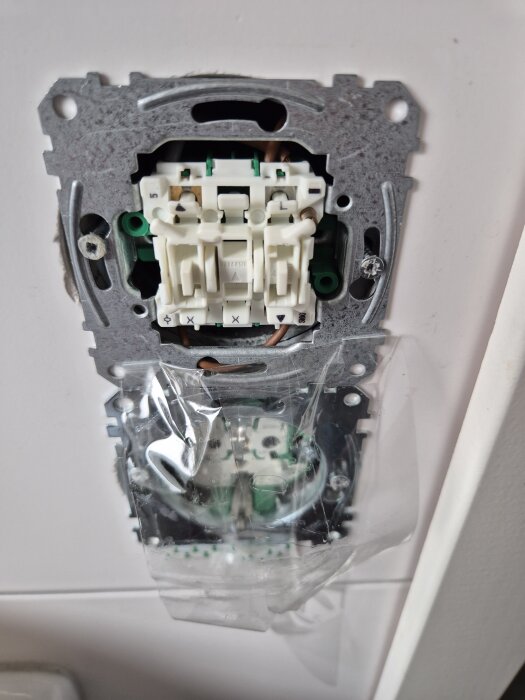 Inbyggd knapp-dimmer i vägg under installation, med synliga ledningar och komponenter inuti metallram.