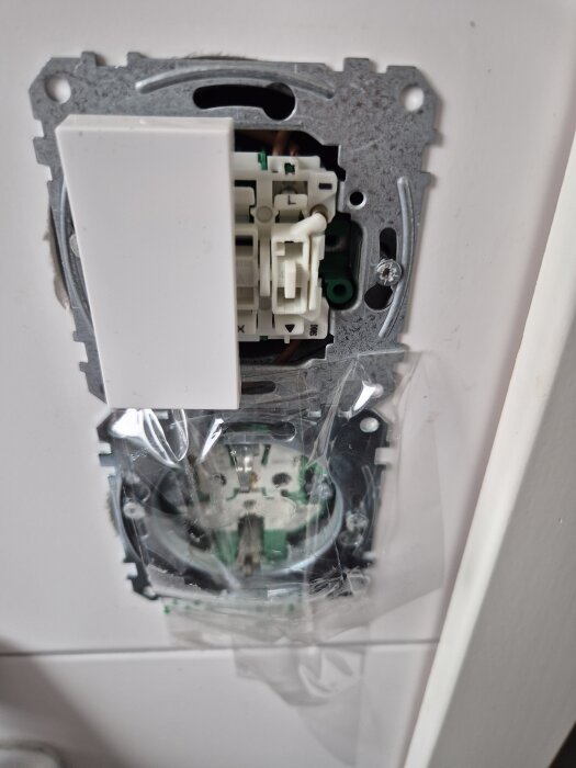 En knapp-dimmer monterad på en vägg, delvis installerad med synliga ledningar och skruvar.