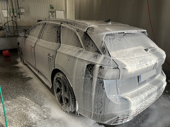 Bil täckt av skum under tvätt i garage, med tvättutrustning i bakgrunden.