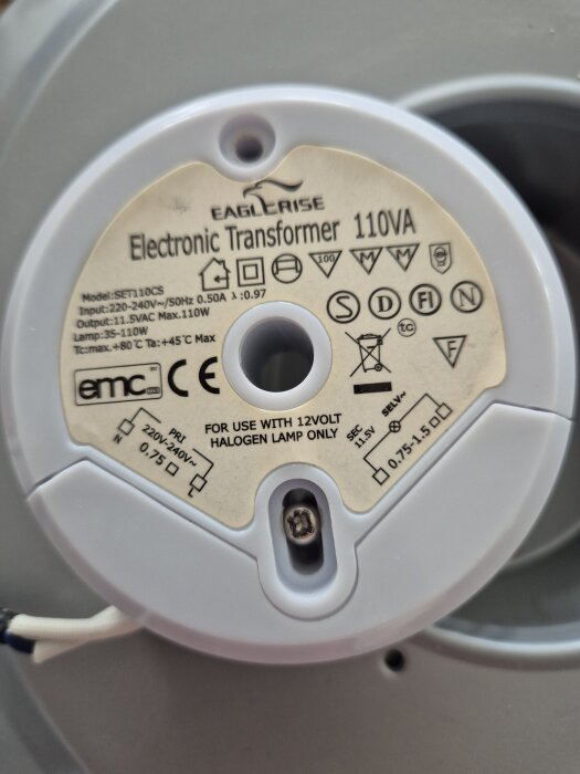 Elektronisk transformator 110VA, modell SET110CS, använd för 12V halogenlampor. Inmatning 220-240V, utmatning 11,5V. Innehåller olika symboler och märkningar.