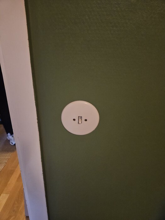 Rund strömbrytare på grön vägg från 60-tal, trasig och svår att ersätta enligt användarens fråga om byte eller elektriker.