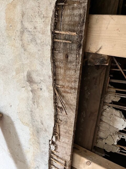 Innervägg med ett område av råspont till höger och en putsad yta till vänster, med reglar synliga bakom.