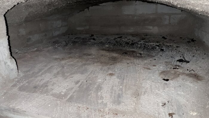 Inuti en bakugn med skrovlig yta och mörka märken på golvet.