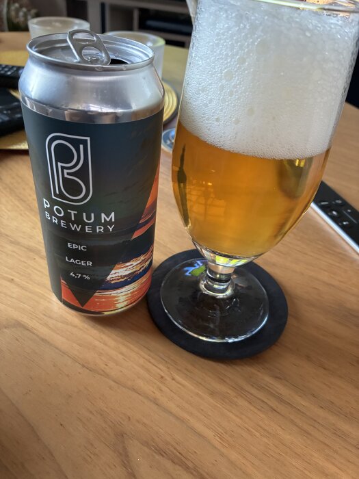 Ölglas med Potum Brewery Epic lager och en öppnad ölburk på ett bord.