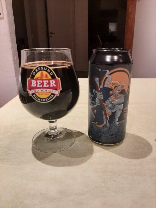 En glas med mörk öl och en burk med motiv av en riddare placerade på ett bord.