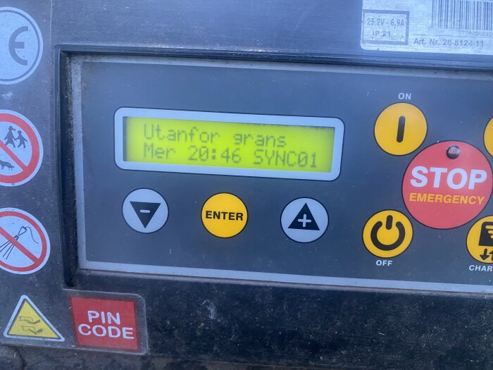 Kontrollpanel med digital skärm som visar "Utanför gräns", gul Enter-knapp och röd "Stop Emergency"-knapp.