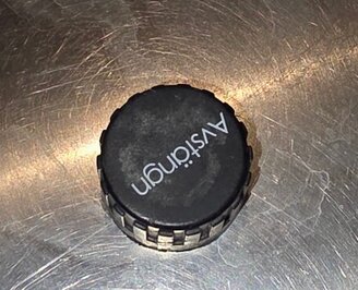 Svart avstängningslock för varmvatten på ventilröret, ligger på en metallisk yta.