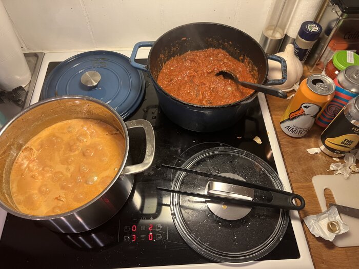 Två grytor på spisen: en med asiatisk gryta och en med chili. Flera dryckesburkar synliga på köksbänken.