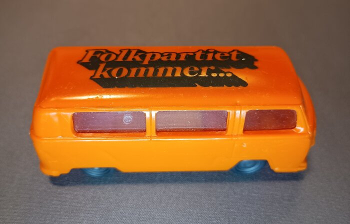 Orange leksaksbil med texten "Folkpartiet kommer..." på taket.