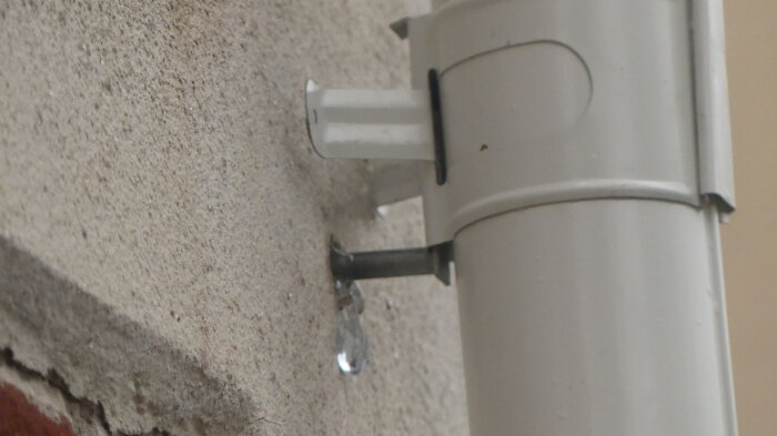Droppande vatten från en vit stupränna monterad mot en putsad vägg.