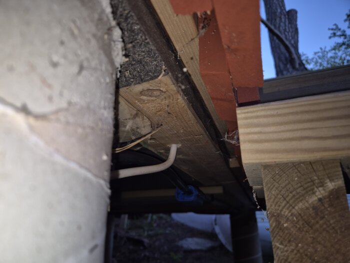 Elektrisk ledning dragen under en trästruktur, med kabel genom golvbjälken och omgivet av isolering och trädetaljer.