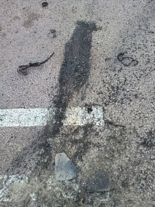Bild av en asfalterad yta med svarta däcksrester och gummidelar kvar efter bilburnout på parkeringsplats.