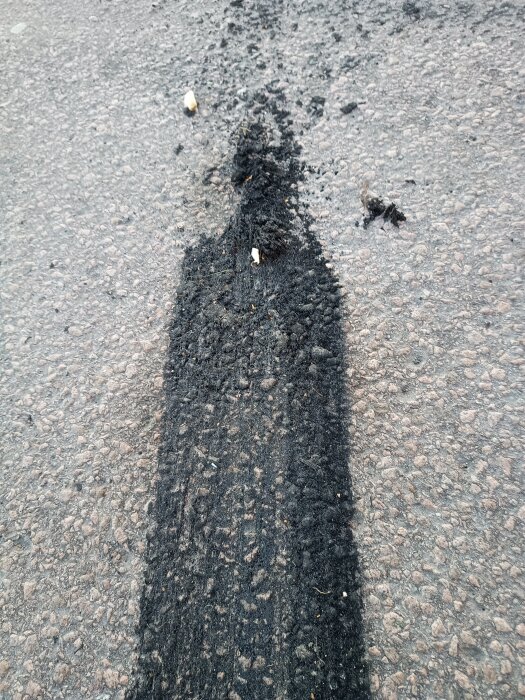 Svarta däckspår på asfalt, troligen från EPA-traktorer, med små skräp på ytan.