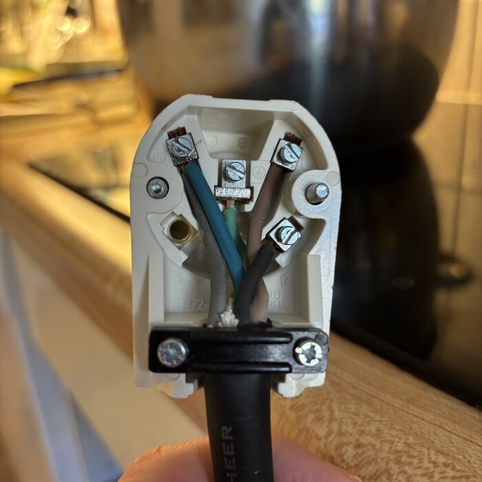 Anslutning av hällens kabel med fyra ledare: blå, brun och gröna samt jordad, fastsatta i en plastkontakt med skruvar.