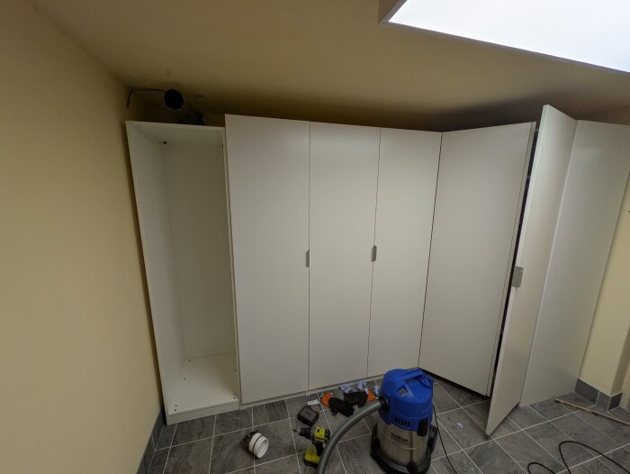 Avsågad Pax-garderob i ett rum med verktyg och dammsugare på golvet, förbereder montering av socklar ovanpå.