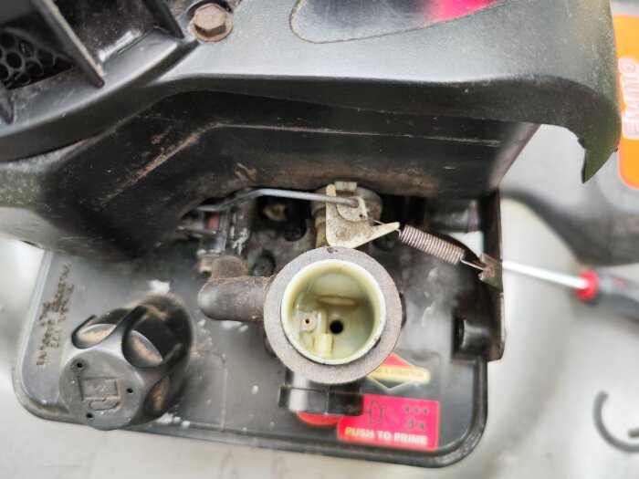 Närbild på en Briggs & Stratton motorfjäder och förgasare, visande delar relaterade till motorprestandaproblem och vibrationer vid tomgång.