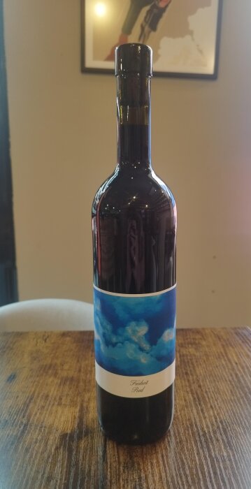 Mörkt vinflaska på träbord med blå etikett, texten "Freiheit Red".