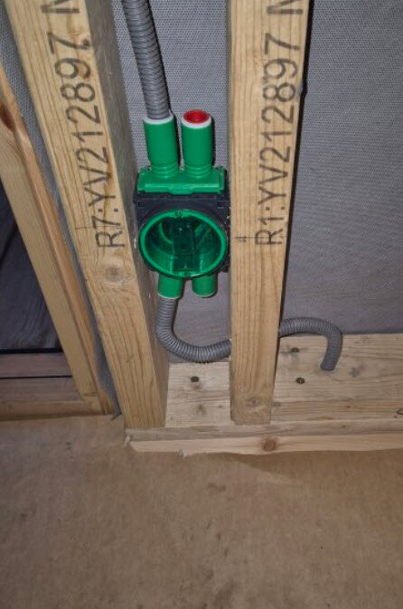 En grön elcentral installerad i en träram av reglar, med rör som böjs runt för montering.