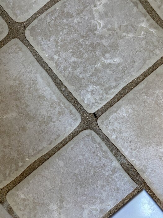 Spricka i golvfog mellan ljusa kakelplattor i dusch, möjlig fuktskada i våtskiktet i ett äldre 50-talshus.