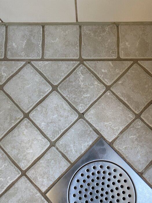 Kaklat golv i dusch med en liten spricka i fogen, silverfärgad golvbrunn synlig i hörnet.