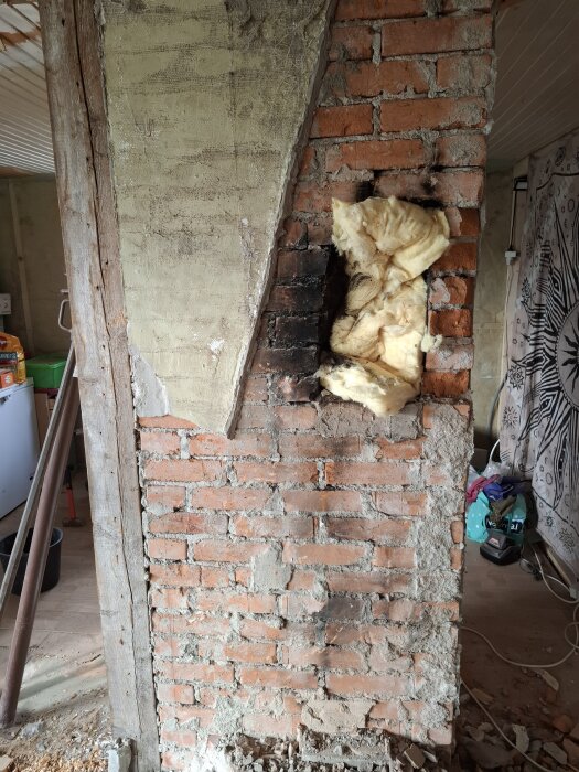 Tegelvägg med sotfläckar och isoleringsmaterial synligt; murstocken ska putsas.