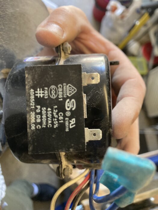 En hand håller en kondensator märkt "CBB61" med specifikationen 1-2µF, 450VAC, 50/60Hz.