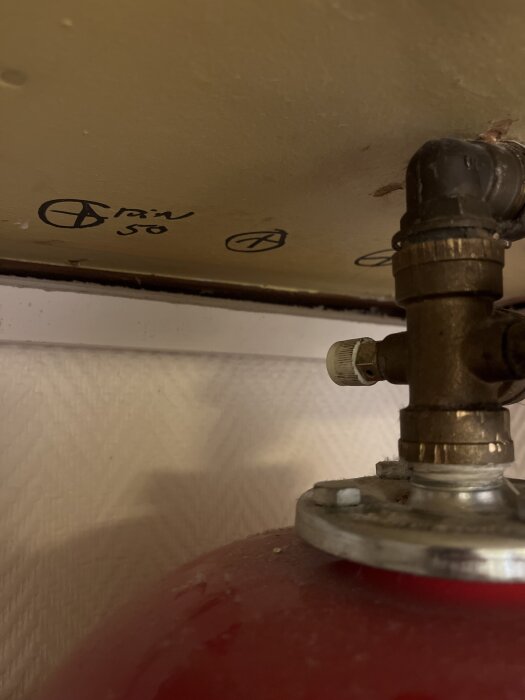 Vinkelventil med vit ratt vid röranslutning, potentiell vatteninloppspunk. Märkt med text och symboler på gul bakgrund.