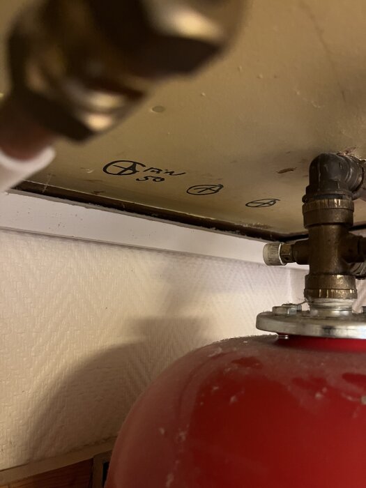 Röd trycktank med ventiler, en vit komponent syns baktill.