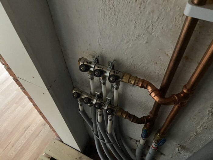 Rörsystem för värme med kopparledningar och märkta ventiler i en villa från 1960-talet, potentiellt för inspektion inför värmesystembyte.