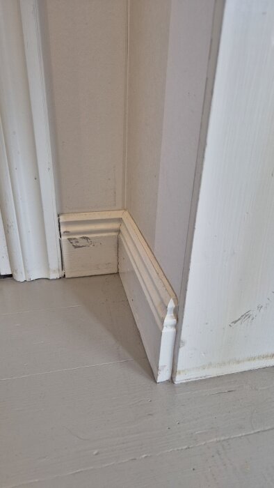 Vit golvsockel i ett hörn med slitage efter golvslipning.