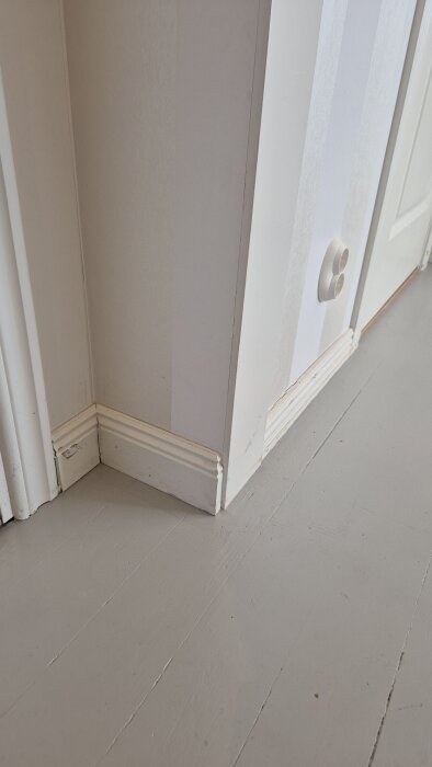 Vita väggsocklar och foder i ett rum, visar skador från golvslipning med behov av ommålning.