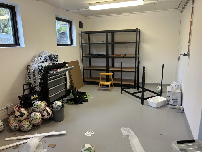 Nyrenoverat garage med lagerhyllor under uppbyggnad, verktygslåda, fotbollar och byggmaterial på golvet.