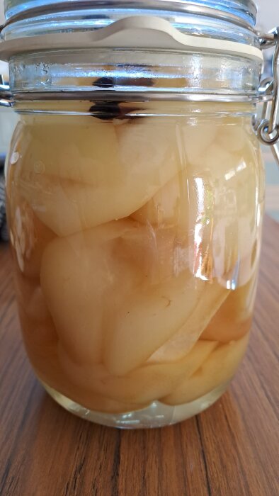 Inlagda päron av sorten Fritjofar med kanel och ingefära i en glasburk på ett bord.