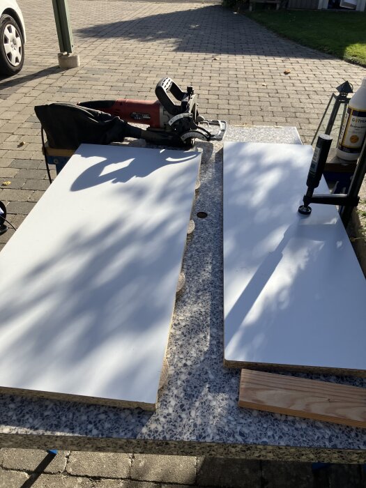 Två vita hyllplan och en röd handöverfräs på ett utomhusbord för träbearbetning.