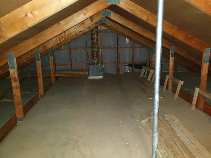 Bild av en vind med exponerade takbjälkar, förbättrad isolering längs sidorna och en smal gång av brädor i mitten.