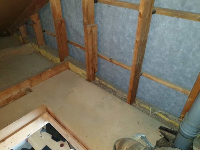 Bild av vind med träreglar, isolering och plattform för förvaring. Synlig glasfiberull längs väggen och liten gång i mitten.